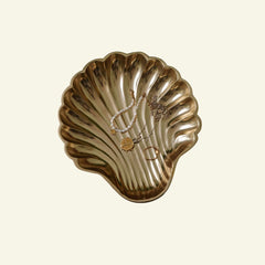 Gold shell-shaped jewelry dish with necklaces on a beige background