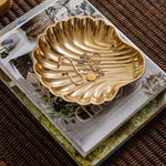 Gold shell-shaped jewelry dish on a magazine with jewelry inside