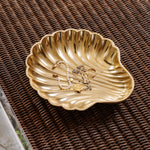 Gold shell-shaped jewelry dish with necklaces on a woven surface