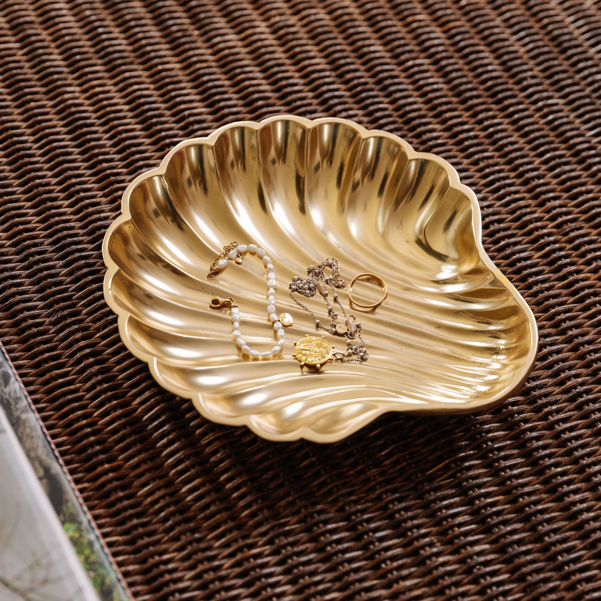 Gold shell-shaped jewelry dish with necklaces on a woven surface