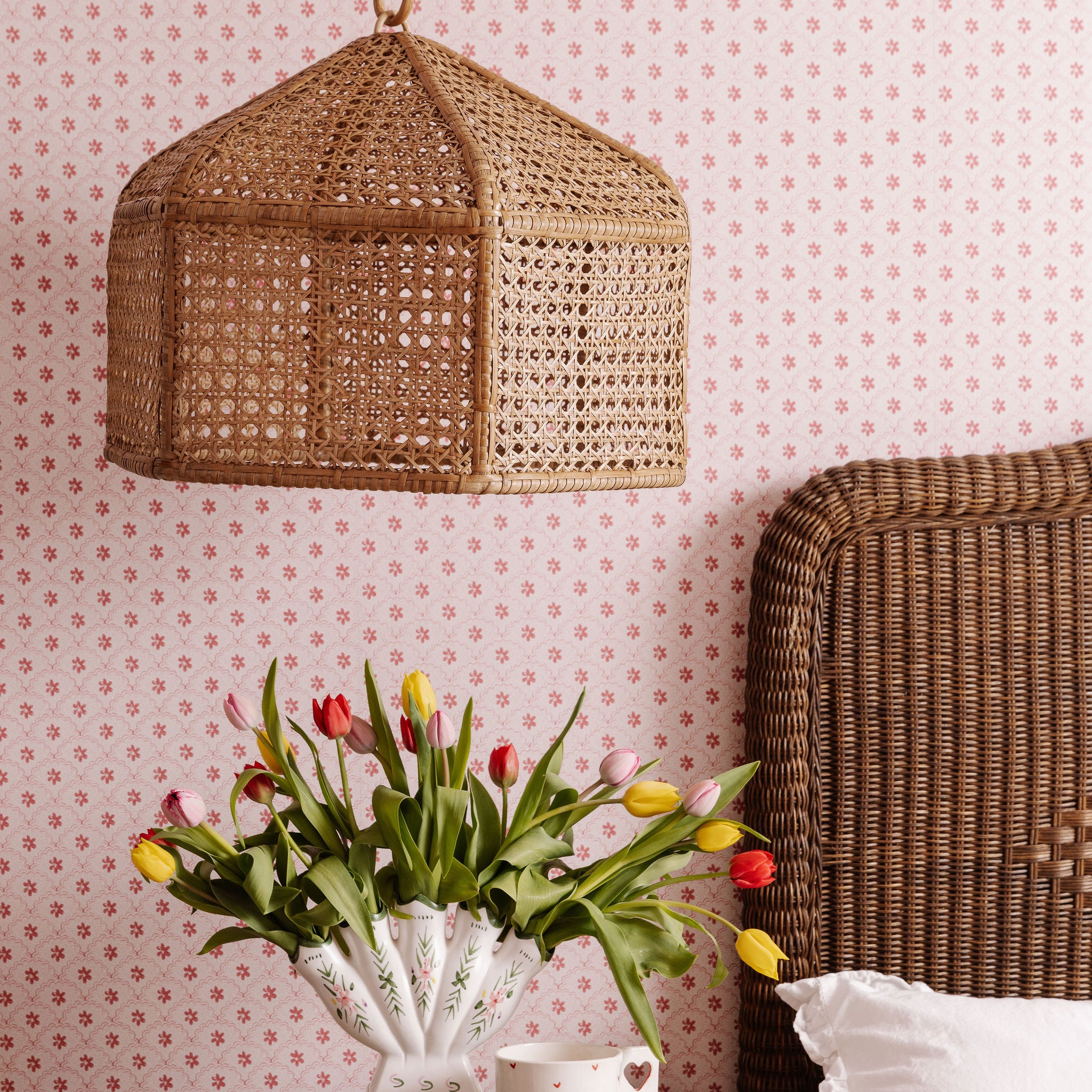 Birdie Wicker lampshade, vase with tulips, and wicker headboard against a floral wallpapered wall.