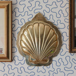 Decorative brass shell wall art on a patterned wall with framed pictures.