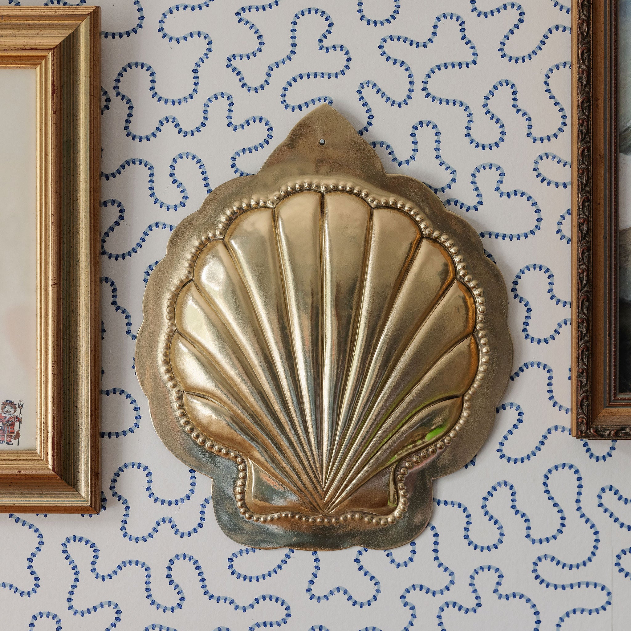 Decorative brass shell wall art on a patterned wall with framed pictures.
