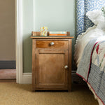 Wooden nightstand next to a bed with a floral curtain in a bedroom setting
