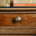 Wooden drawer with a metal knob on a shelf with books in the background