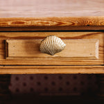 Wooden drawer with a shell-shaped brass handle on a wooden surface.