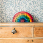 Colorful rainbow-shaped object on a wooden dresser with patterned wallpaper.
