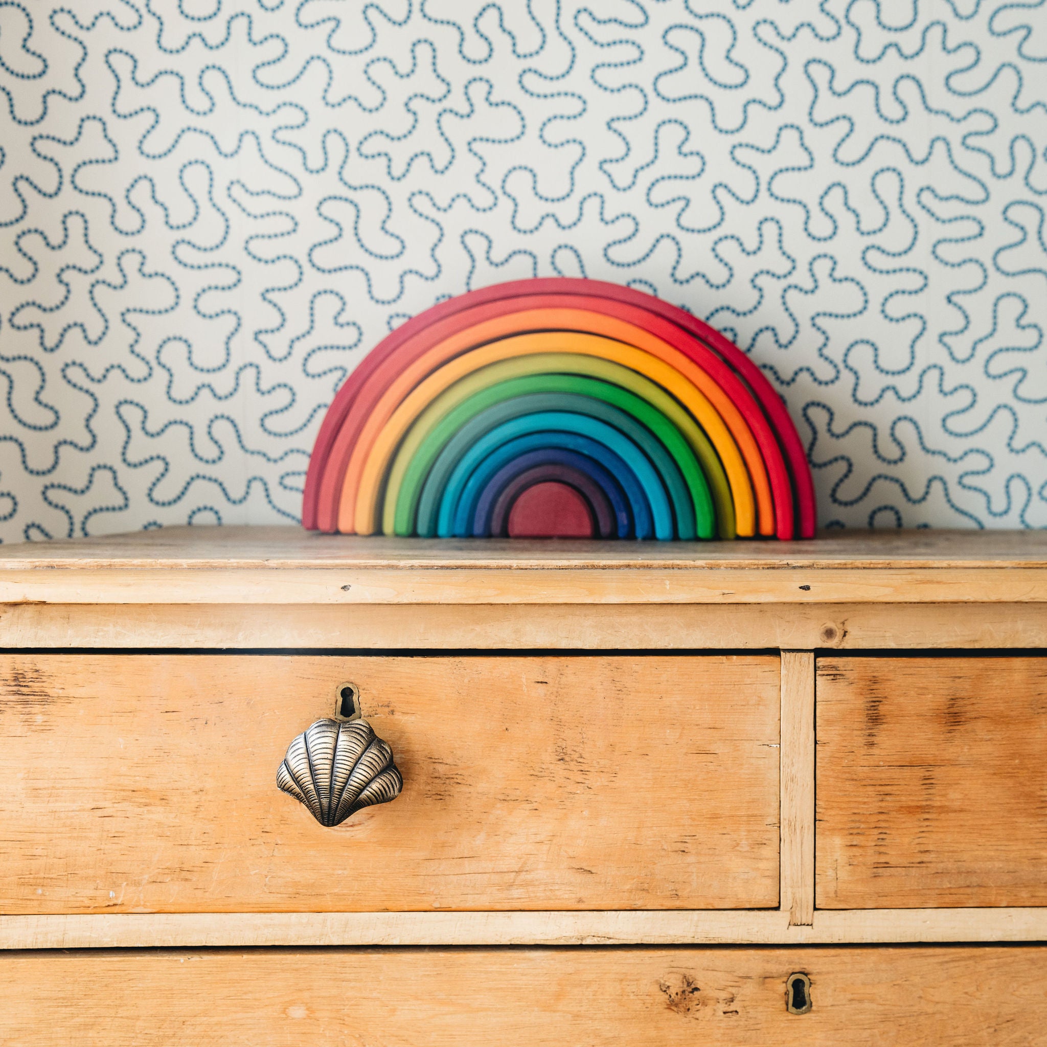 Colorful rainbow-shaped object on a wooden dresser with patterned wallpaper.