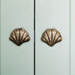 Curved Shell-shaped brass cabinet knobs on a light green cabinet.