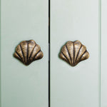 Curved Shell-shaped brass cabinet knobs on a light green cabinet.