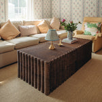 Living room with a Daisy wicker coffee table, beige sectional sofa, and armchair.