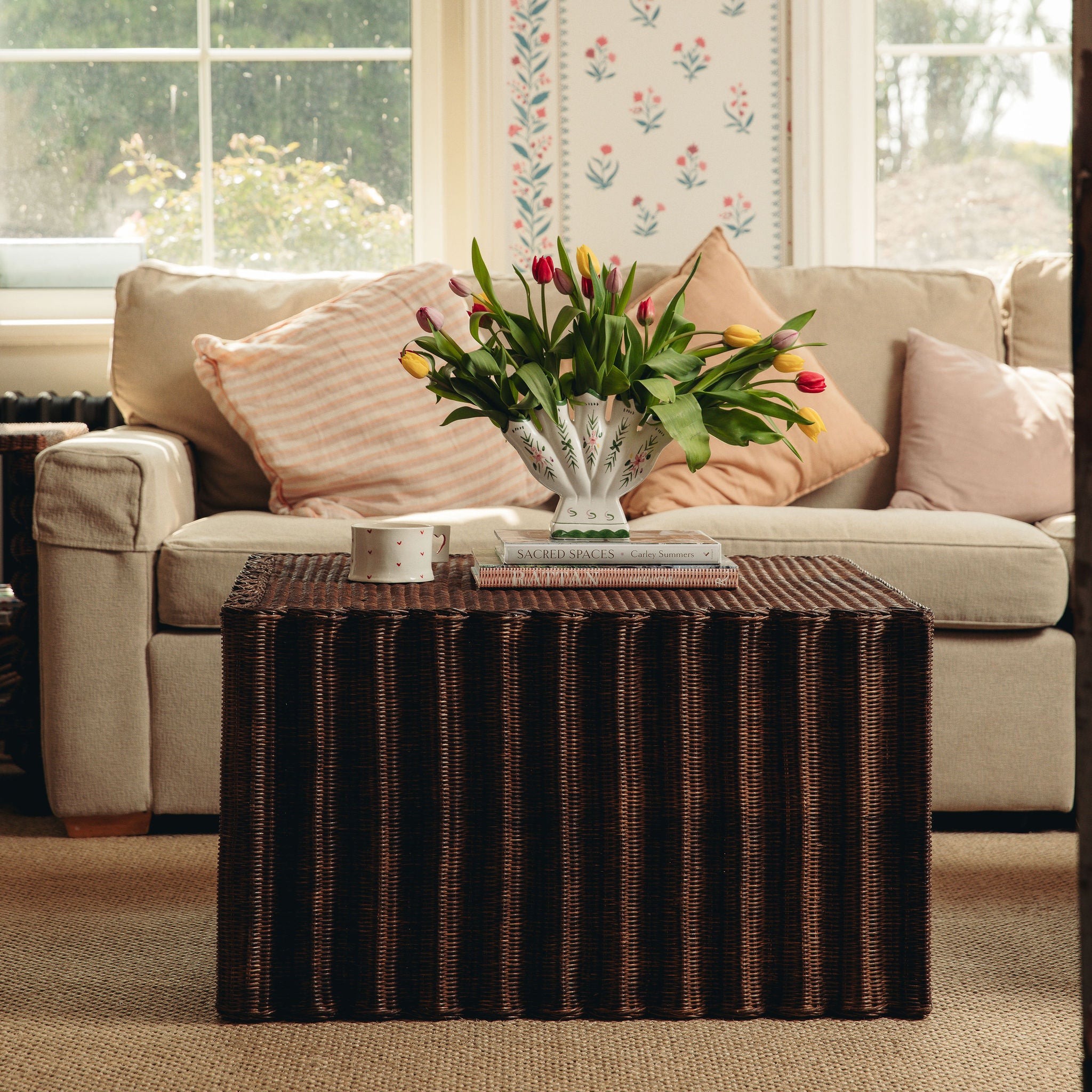 Living room with a beige sofa, Daisy wicker coffee table, and floral arrangement.