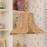 Daphne Woven rattan lampshade hanging against a decorative wall with floral patterns.