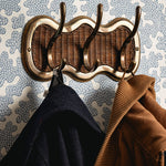 Decorative wicker coat rack with two jackets hanging on it against a patterned wall.