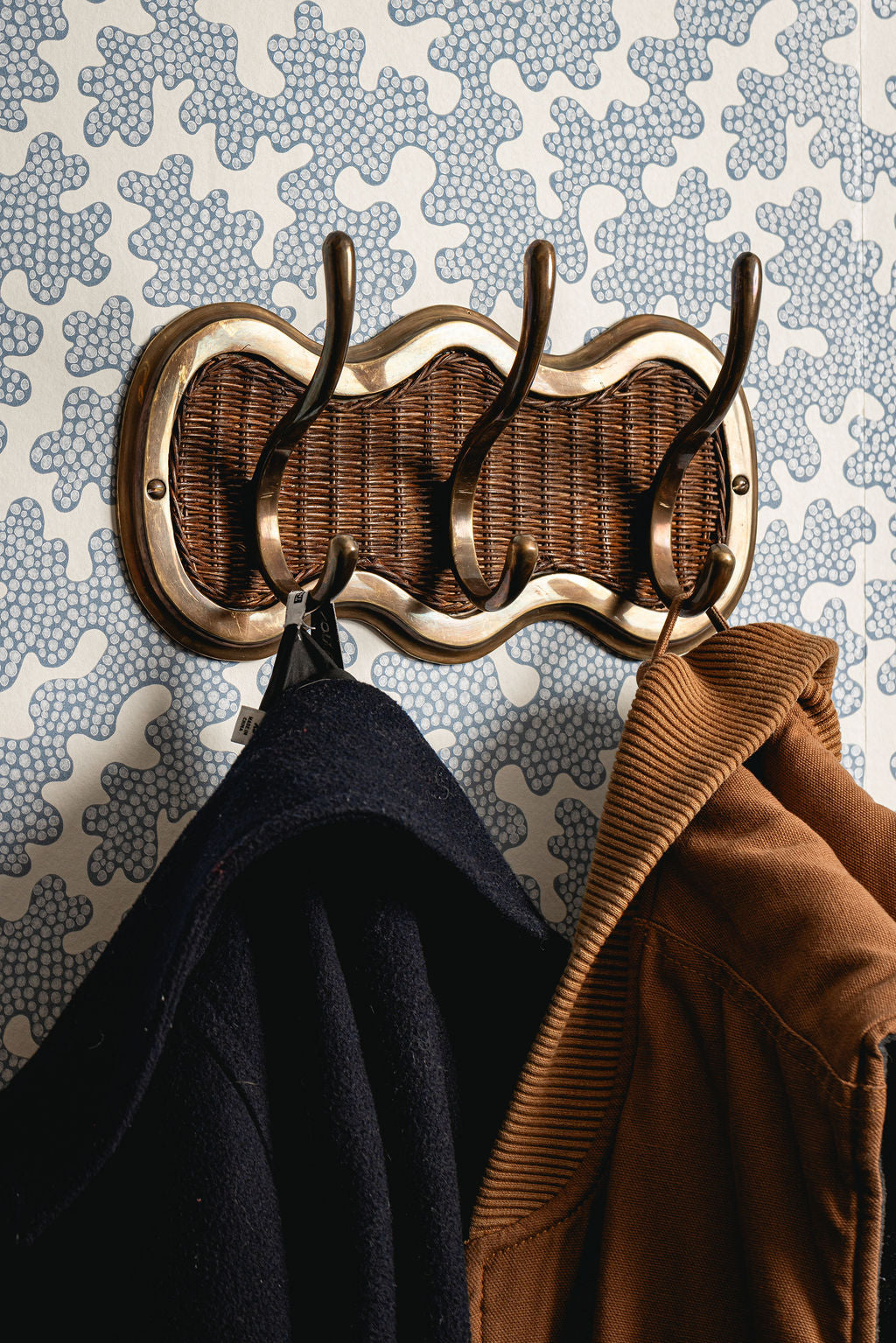 Decorative wicker coat rack with two jackets hanging on it against a patterned wall.