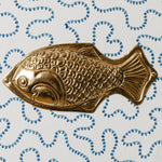 Gold fish-shaped object on a white background with blue wavy patterns