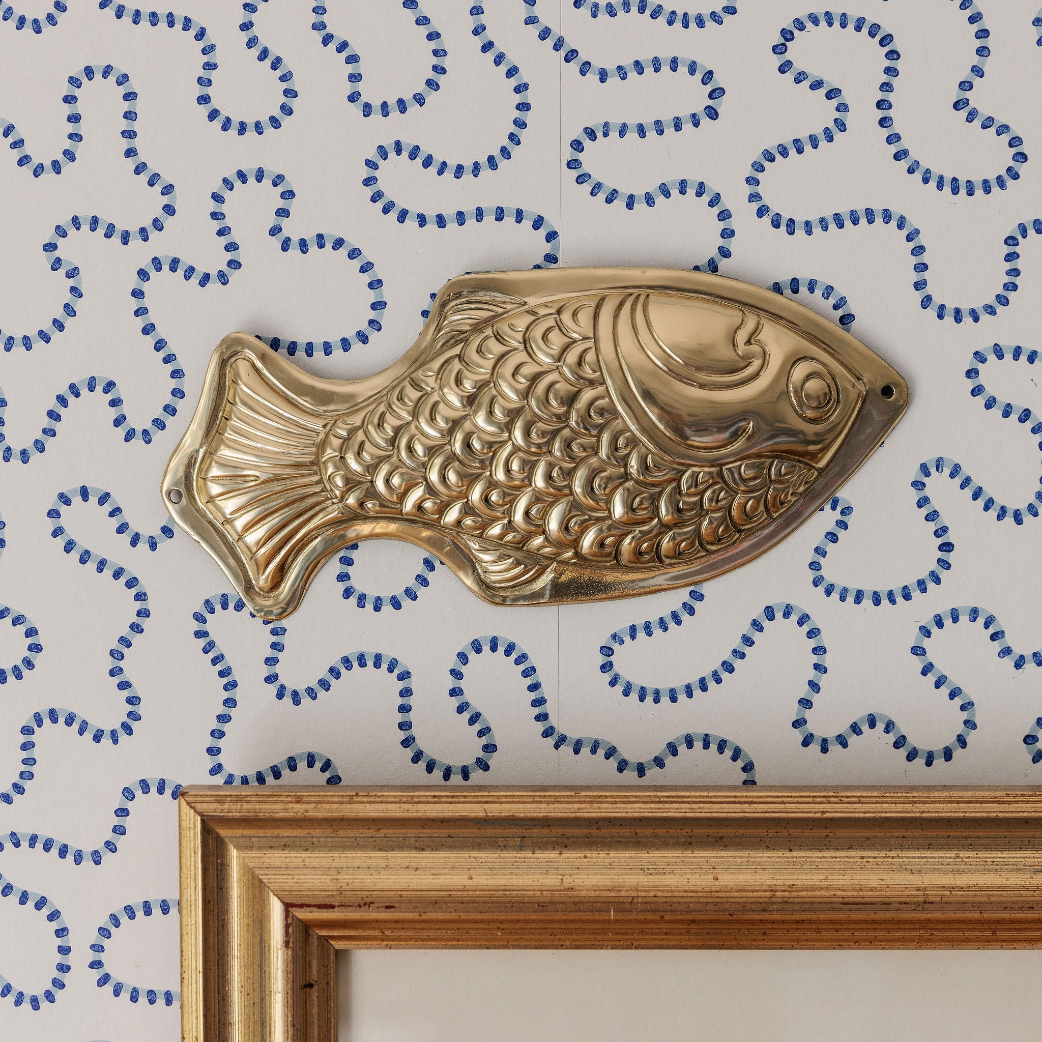 Gold fish-shaped object on a wall with decorative blue patterns