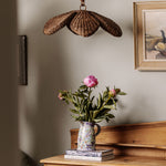 Floral arrangement in a vase on a wooden surface with a shell-shaped lamp and framed picture in the background.