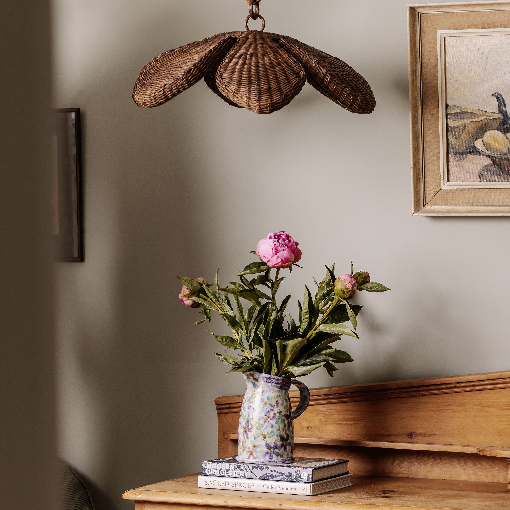 Floral arrangement in a vase on a wooden surface with a shell-shaped lamp and framed picture in the background.