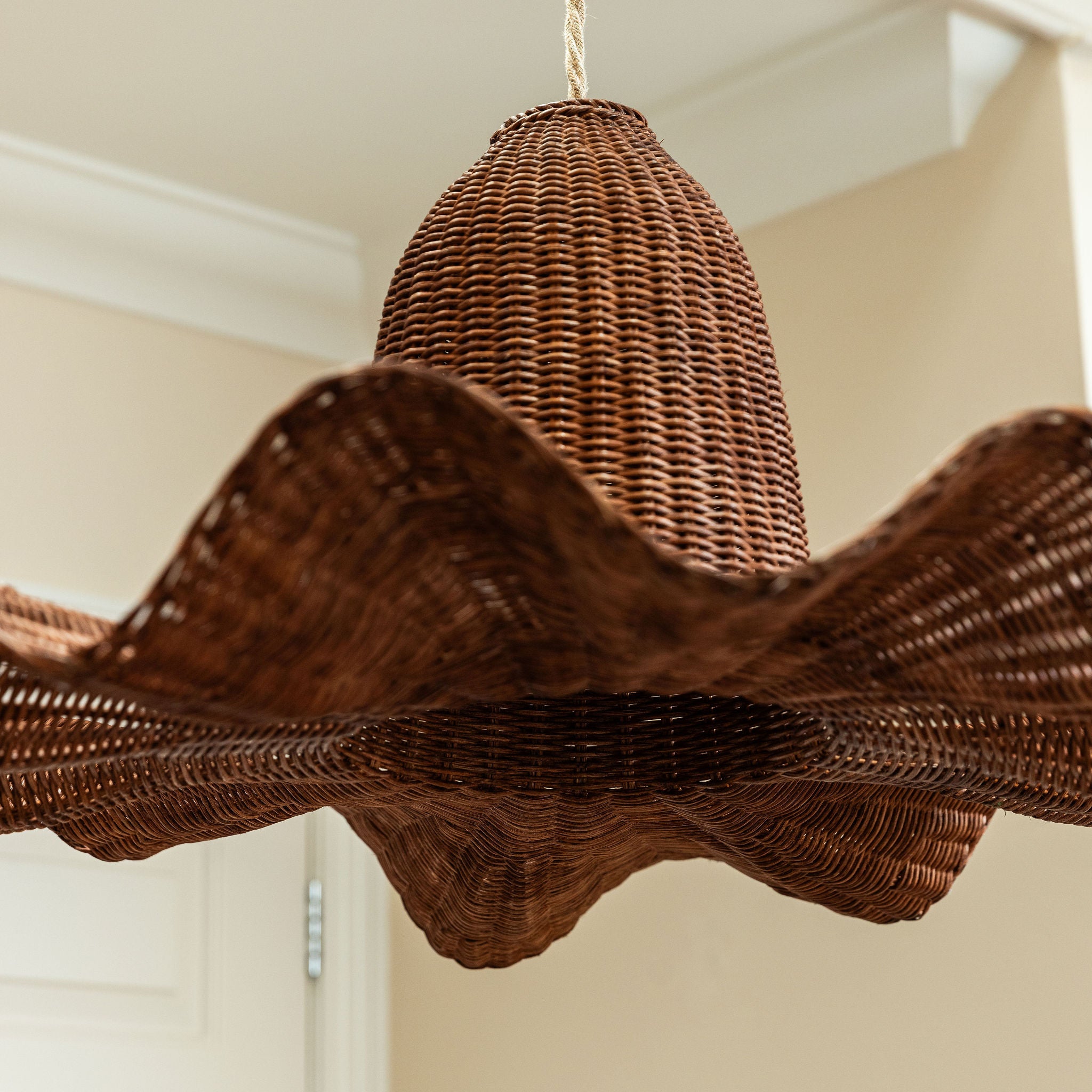 Wicker chandelier hanging from the ceiling in a room with beige walls.