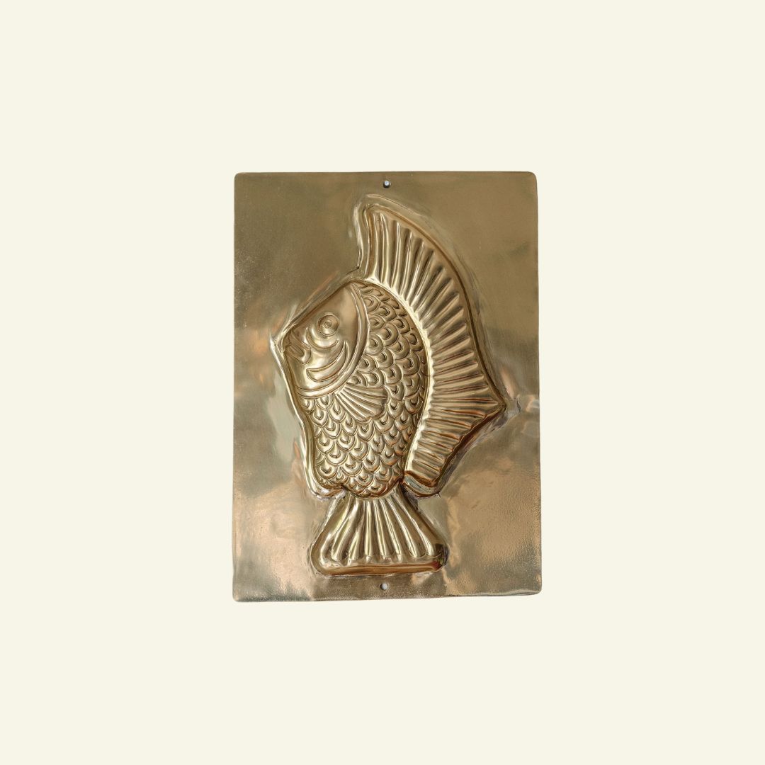 Brass fish-shaped mold on a beige background