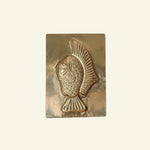 Brass fish-shaped mold on a beige background