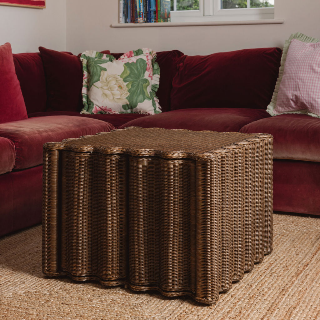 Wicker coffee table in front of a red sofa with decorative pillows.