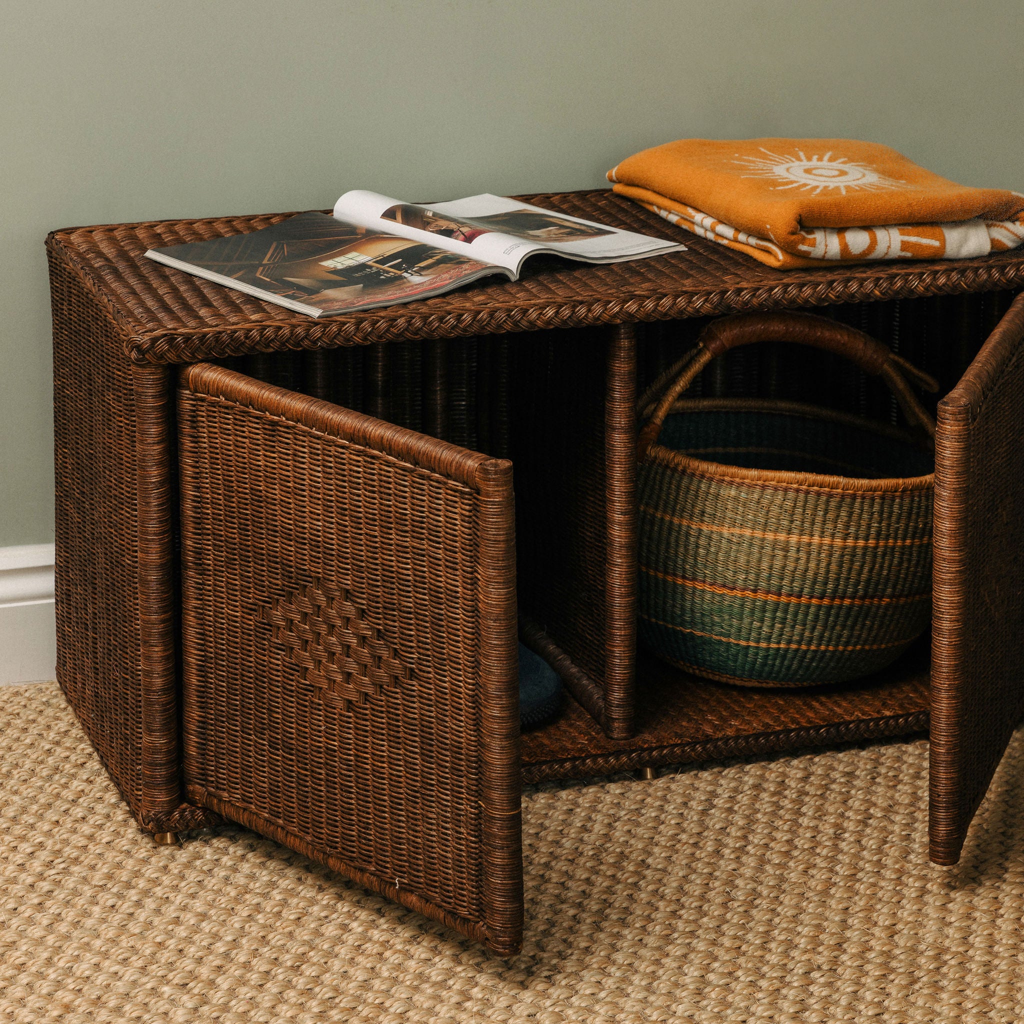 Wicker storage bench with open magazine and folded clothes on a neutral background