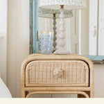 Wicker nightstand with lamp and decorative item in a room setting