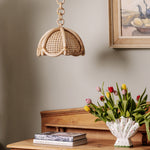 Riviera Rattan pendant light above a wooden table with tulips and books against a neutral wall.