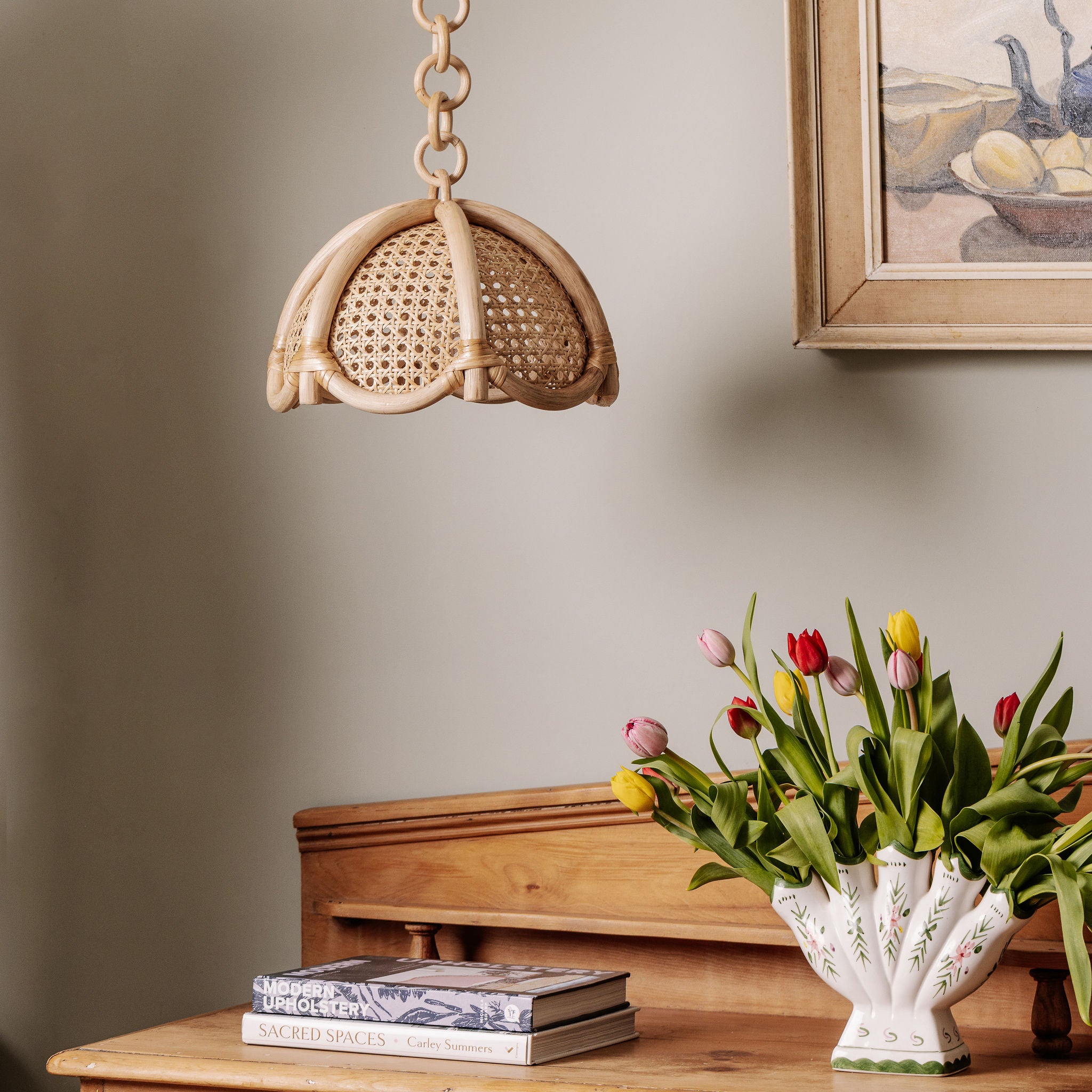 Riviera Rattan pendant light above a wooden table with tulips and books against a neutral wall.
