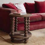 Wicker bobbin side table with a red mug and book in front of a red sofa.