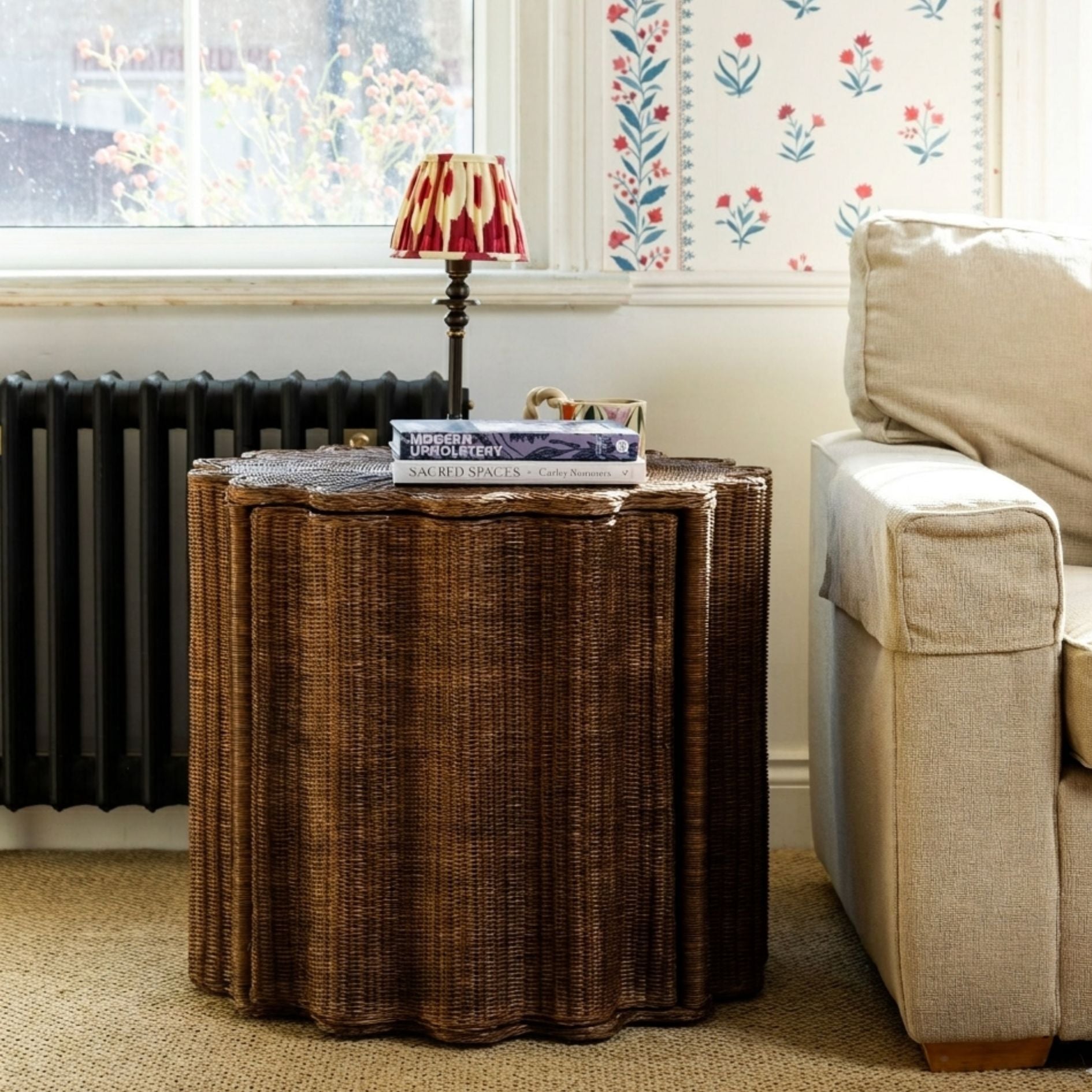 Ruby Wicker side table with books and a lamp next to a beige sofa in a living room.