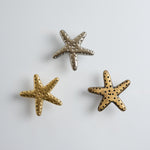 Three starfish-shaped knobs, one gold and one silver, on a light gray background.