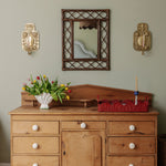 Wooden dresser with decorative mirror and wall sconces against a light green wall.