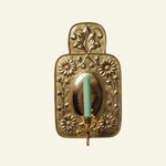 A brass wall sconce with floral patterns and a central turquoise glass holder, featuring a single candle holder on the right side.