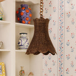 Calla Wicker pendant hanging in front of a shelf with decorative vases against a floral wallpapered wall.