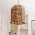 Woven rattan pendant light hanging in a room with floral wallpaper.