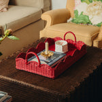 Red wicker tray with a magazine and candle on a dark surface in a living room setting.